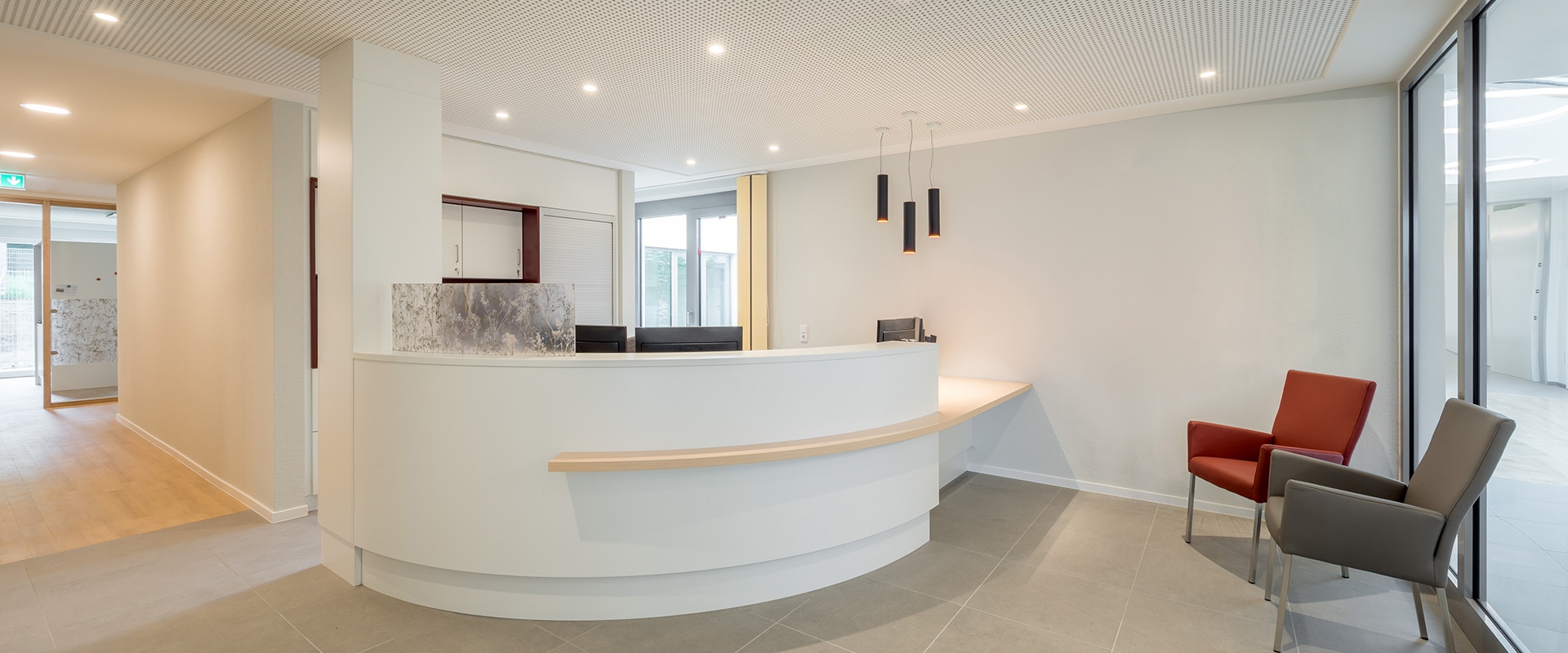 Modern reception area with Artemide Everything 80 Trimless recessed ceiling lights and dark cylindrical pendant lamps above a curved white desk.