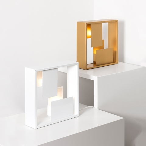 Two Artemide Fato table lamps: one white rectangular frame and one gold square frame, with geometric inner panels diffusing warm light
