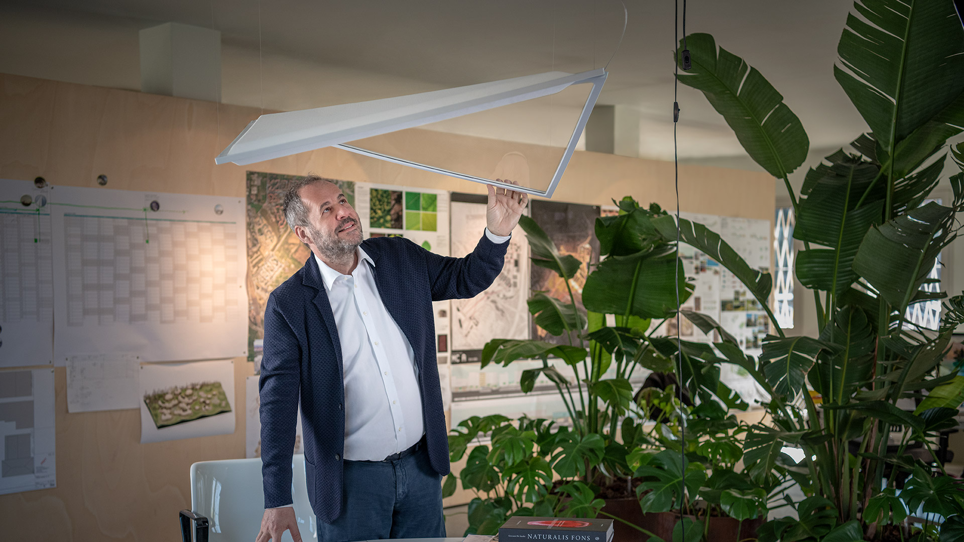 Artemide Flexia triangular pendant and wall lights in white, orange, green, and blue, suspended above a curved white interior space.