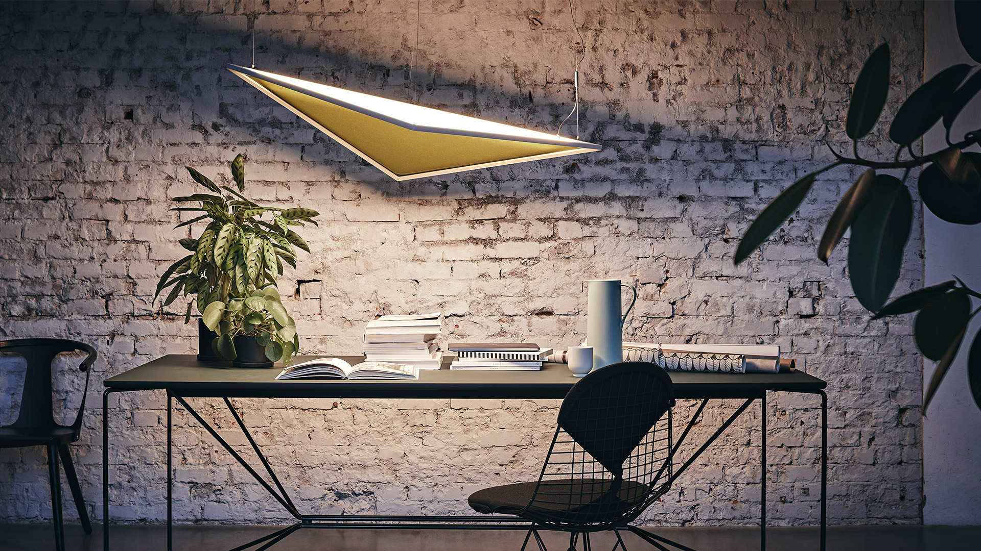 Designer holding an Artemide Flexia slim rectangular LED pendant lamp in a creative studio workspace with plants and design boards