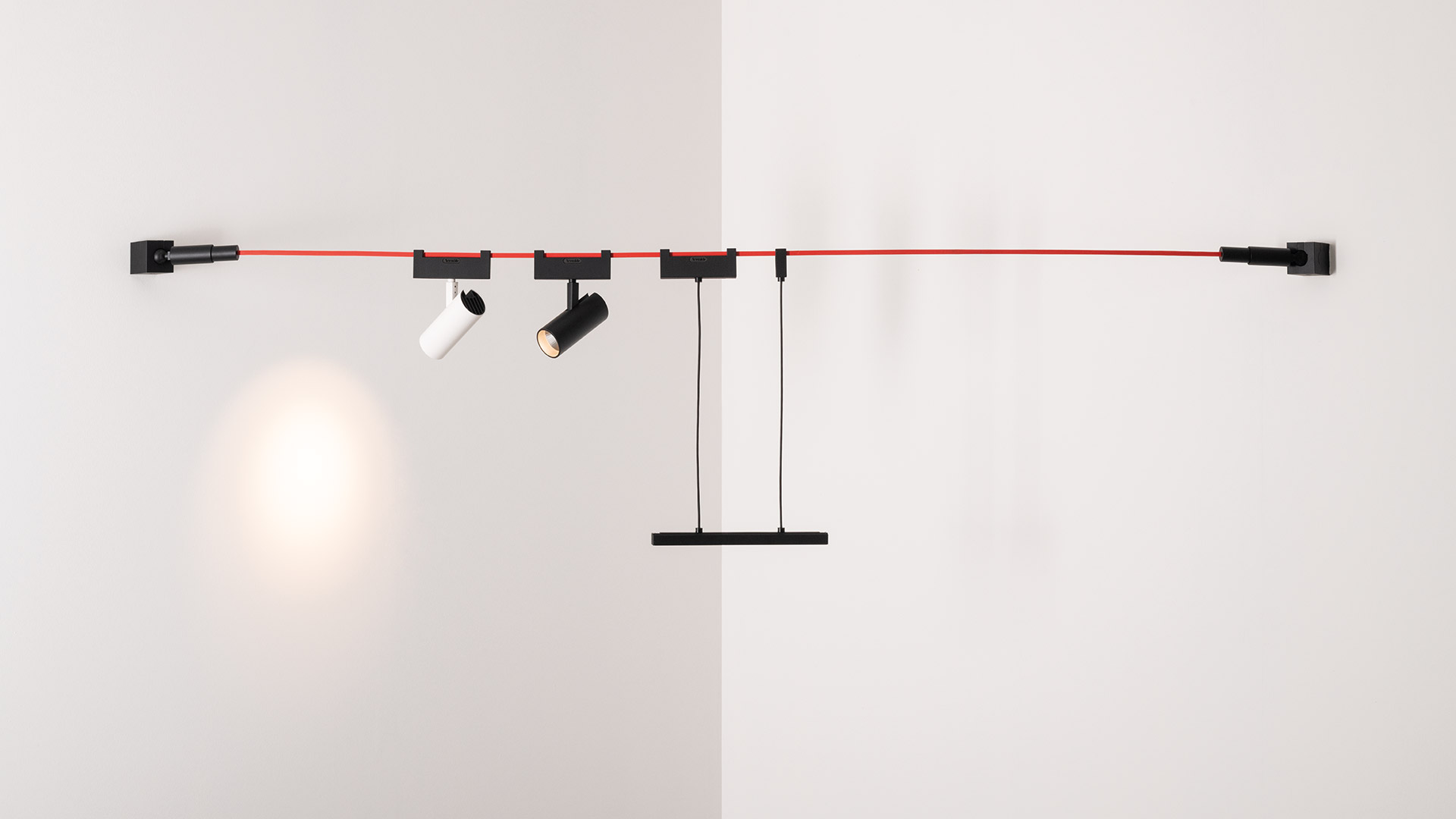 Loft workspace with Artemide Funivia cable lighting system in red and blue, suspending pendant lights over a bar table with stools