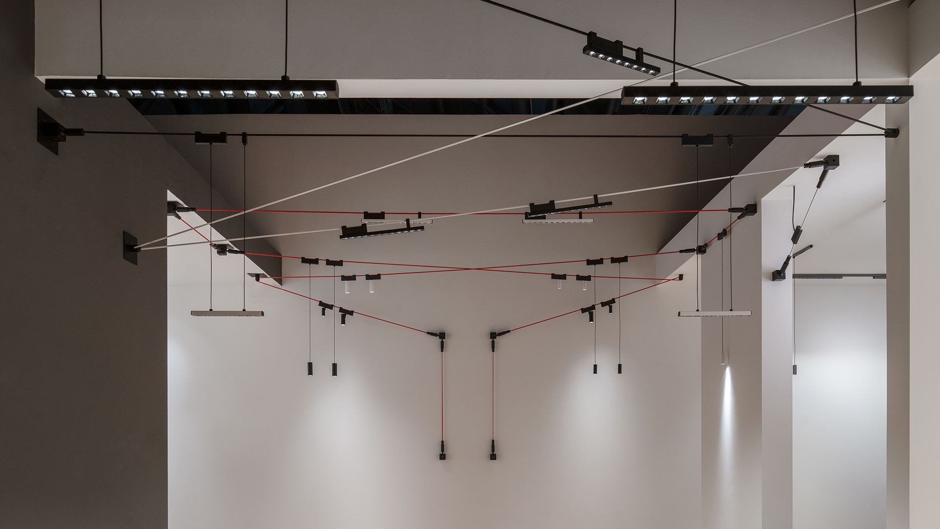 Artemide Funivia: black track system with red cable spanning a wall corner, featuring adjustable spotlights and a pendant bar