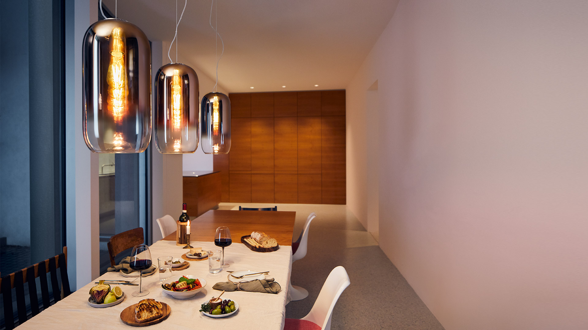 Two Artemide Gople pendant lamps with white glass shades hanging over a bright white modern kitchen island