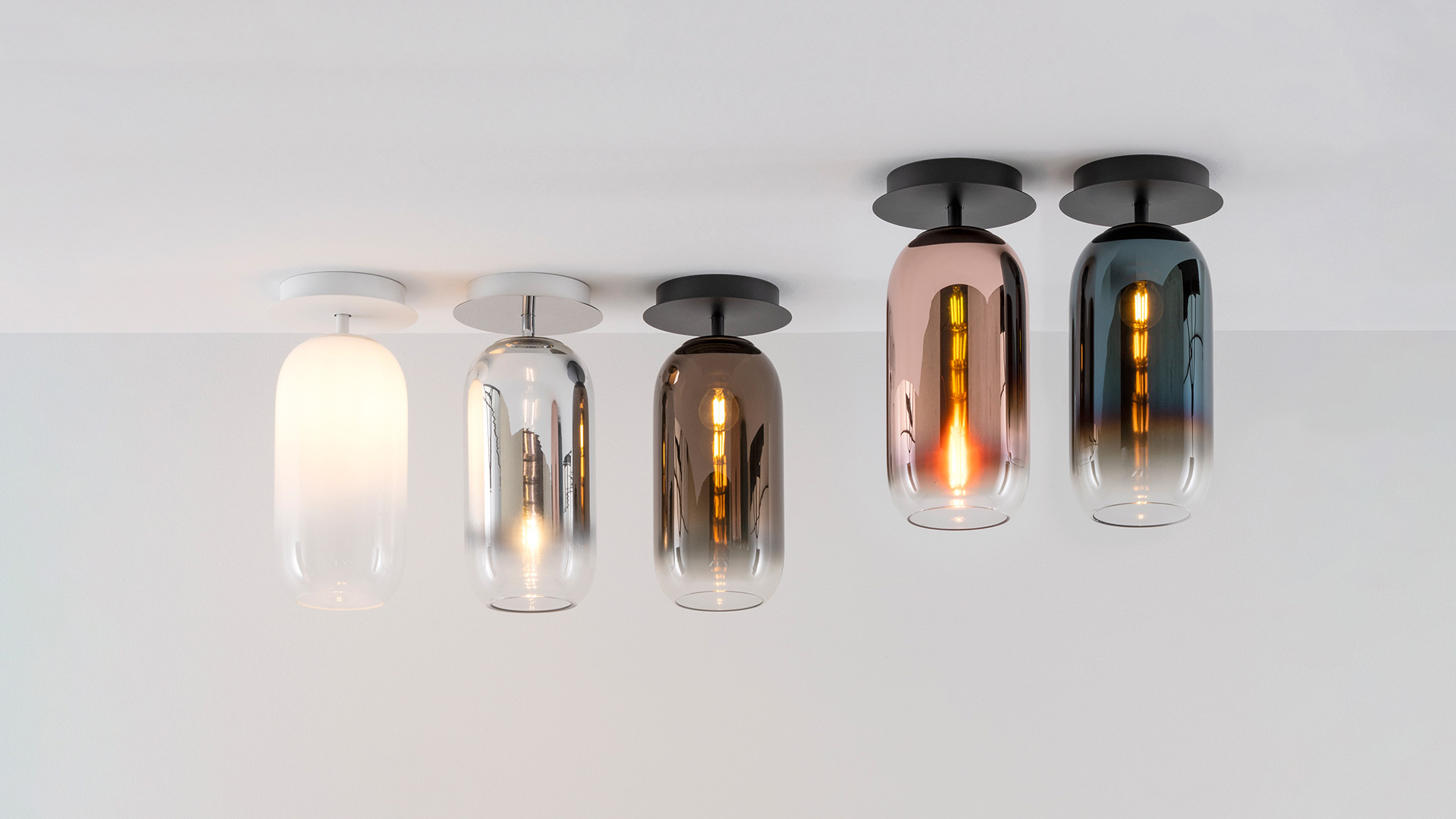 Artemide Gople pendant lamps with smoked glass shades illuminate a modern dining table set for dinner with food and wine.