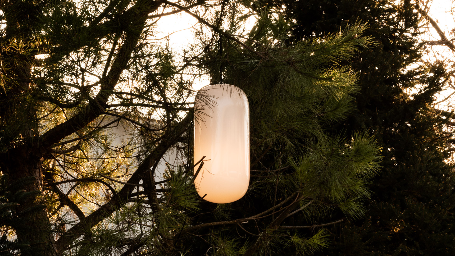 Artemide Gople Outdoor floor lamp with glowing white oval diffuser on wooden stake, placed beside a tree at night near a hammock