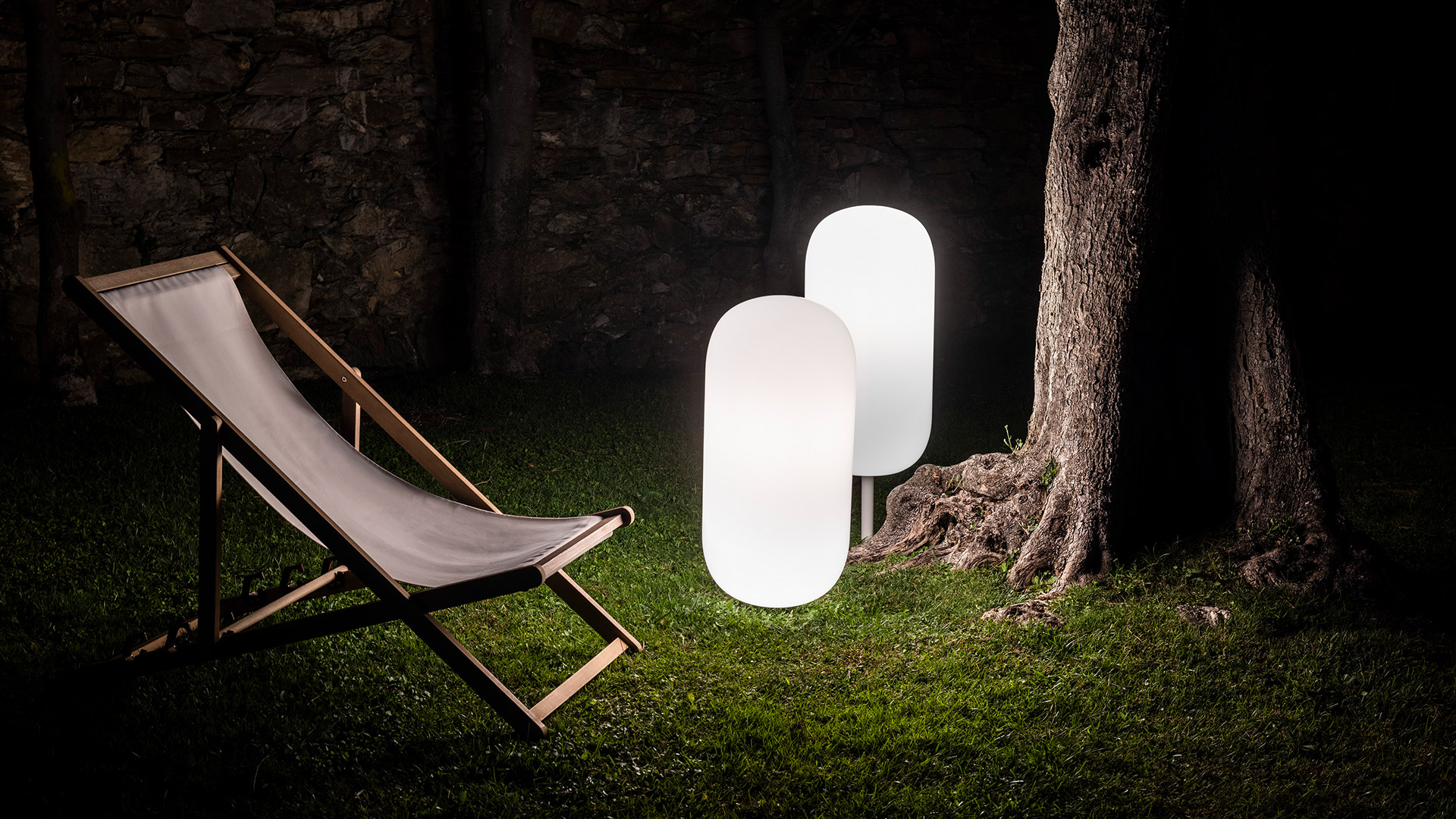 Artemide Gople Outdoor pendant lamp glowing warmly, hanging from pine tree branches at dusk with soft diffused light