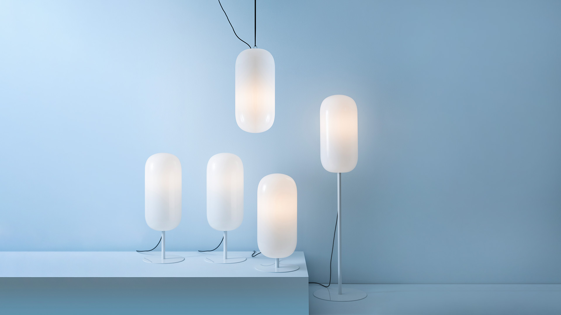 Artemide Gople Outdoor lamp: smooth pebble-shaped white opal diffuser resting on floor, emitting warm glow, with black power cord