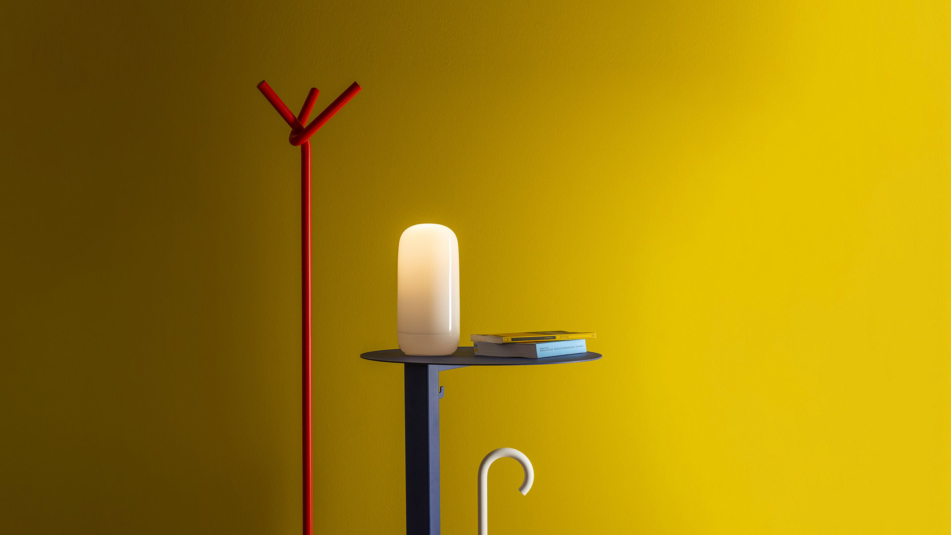 Hand holding the Artemide Gople Portable lamp, a glowing white opal diffuser with a rounded capsule shape.