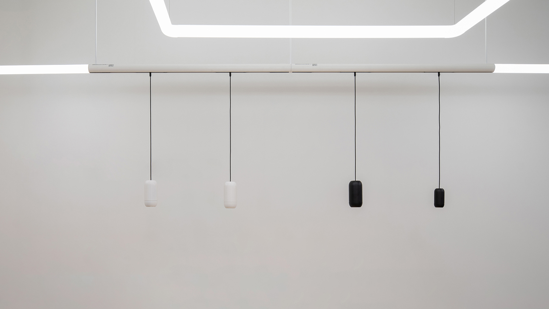 Artemide Gople System: four cylindrical pendants on a white track, two white and two black, hanging from a geometric LED ceiling fixture
