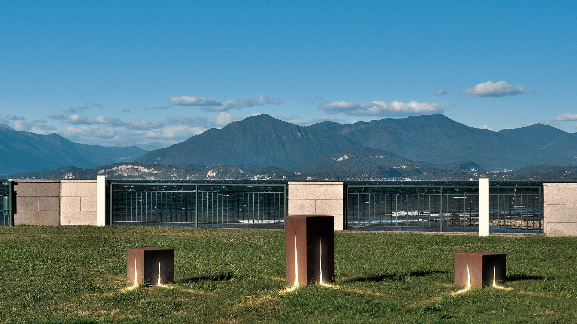 Artemide Granito outdoor installation: dark cubic elements emit intense red light beams across a reflective floor, creating a geometric star pattern.