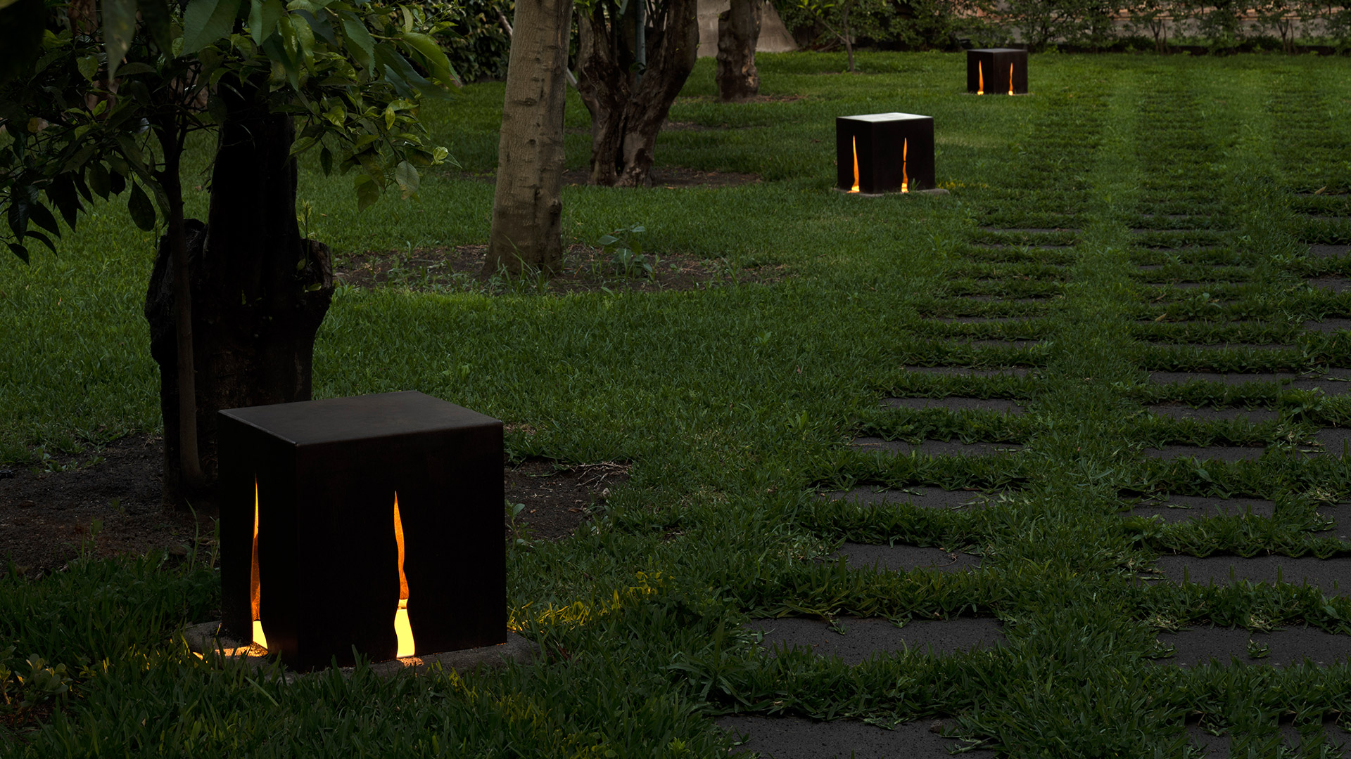Artemide Granito outdoor bollard light in Corten steel, emitting warm light through vertical slits onto surrounding grass