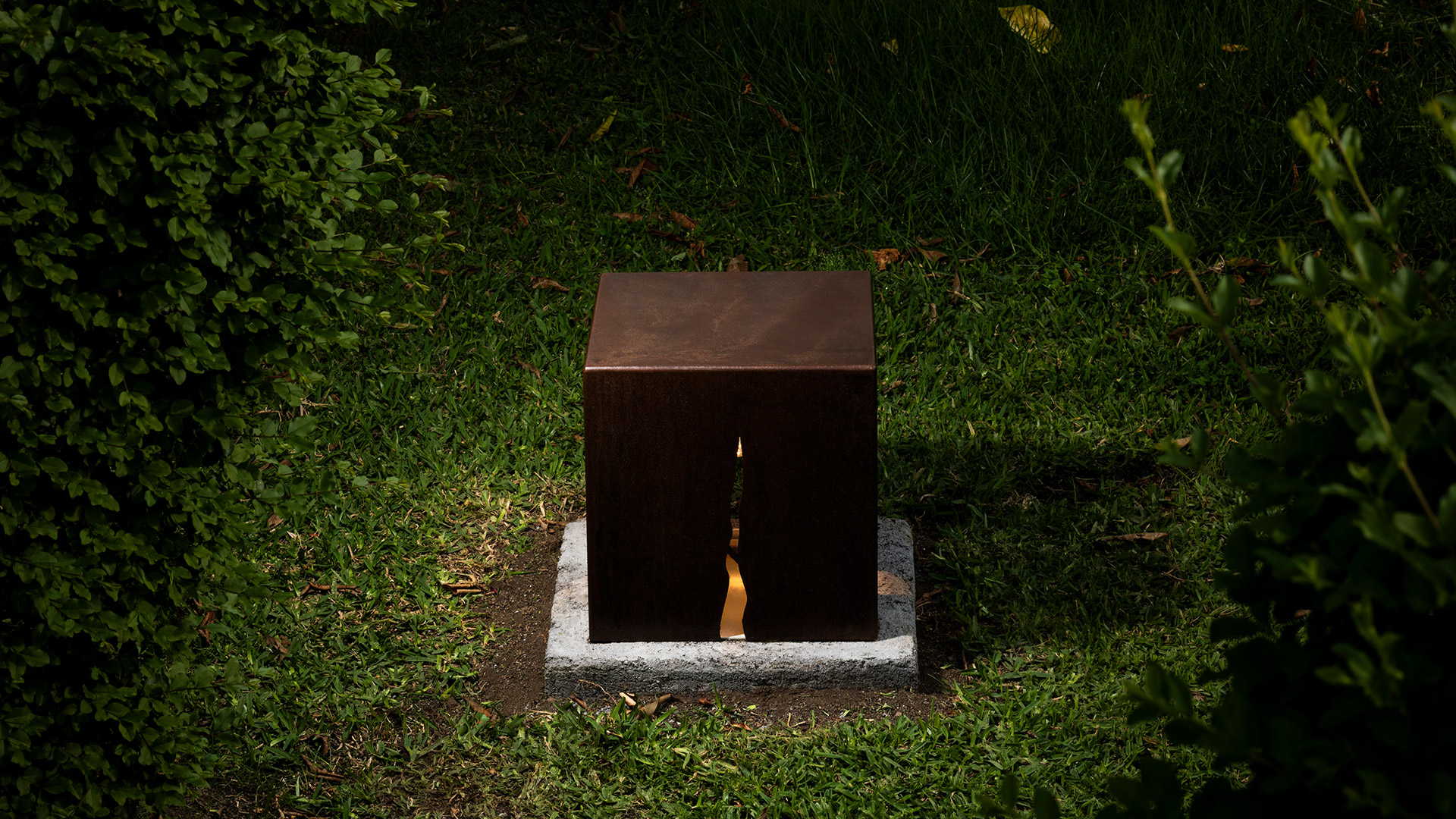 Artemide Granito outdoor lamp: rustic cube-shaped stone fixture on grass, emitting warm light rays extending outward in four directions