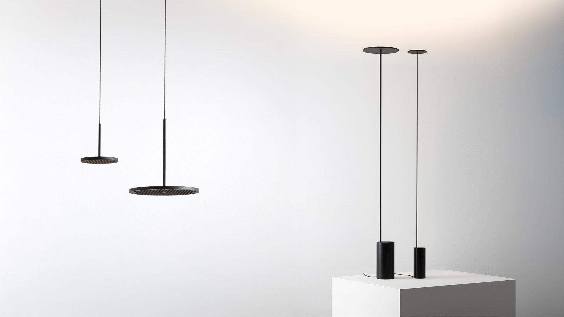 Close-up of Artemide Helgoland floor lamp top: flat circular black disc shade emitting warm ambient light on a slim black stem