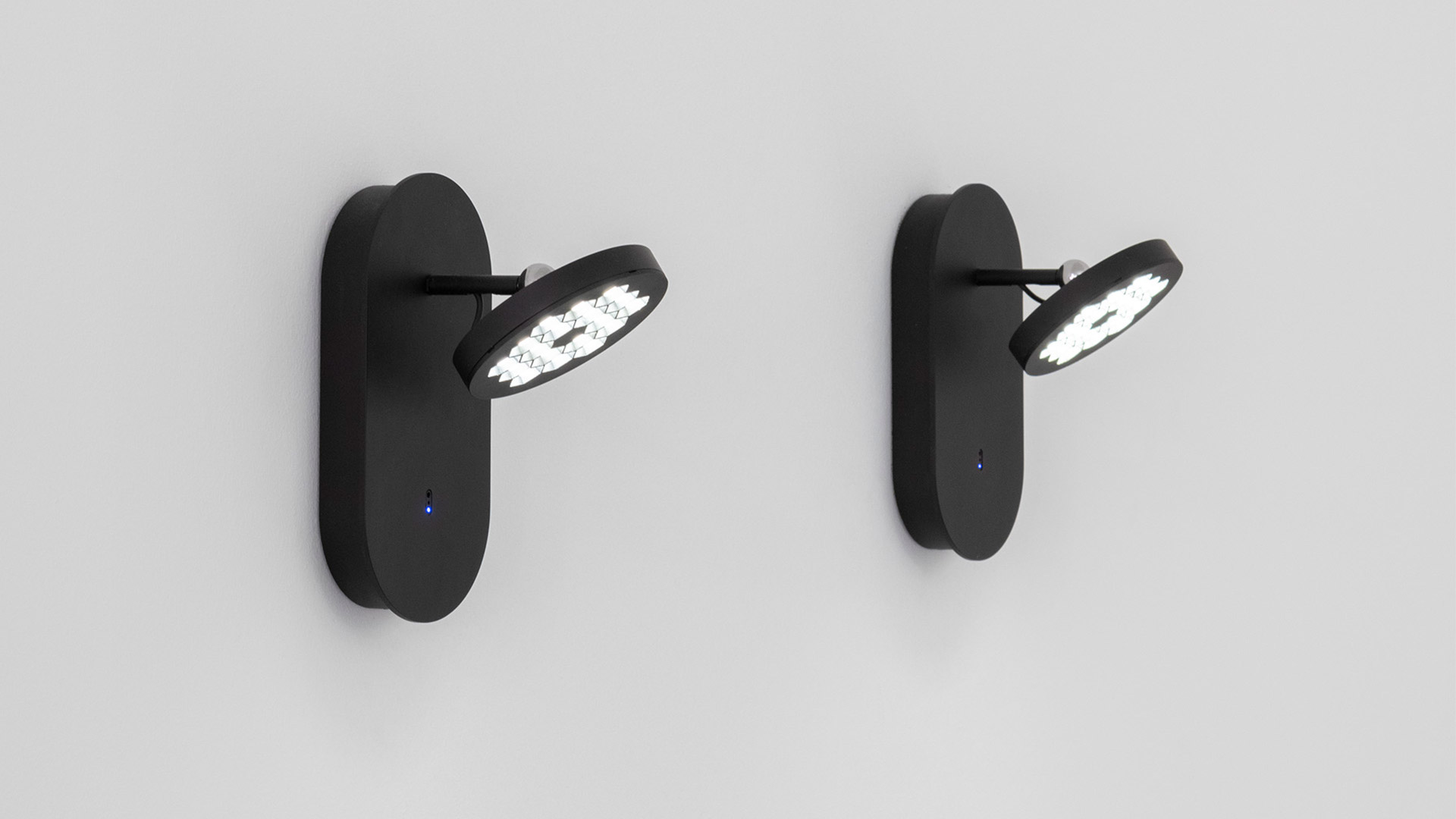 Two Artemide Helgoland wall lights in matte black, featuring circular LED heads on adjustable arms and blue indicator dots
