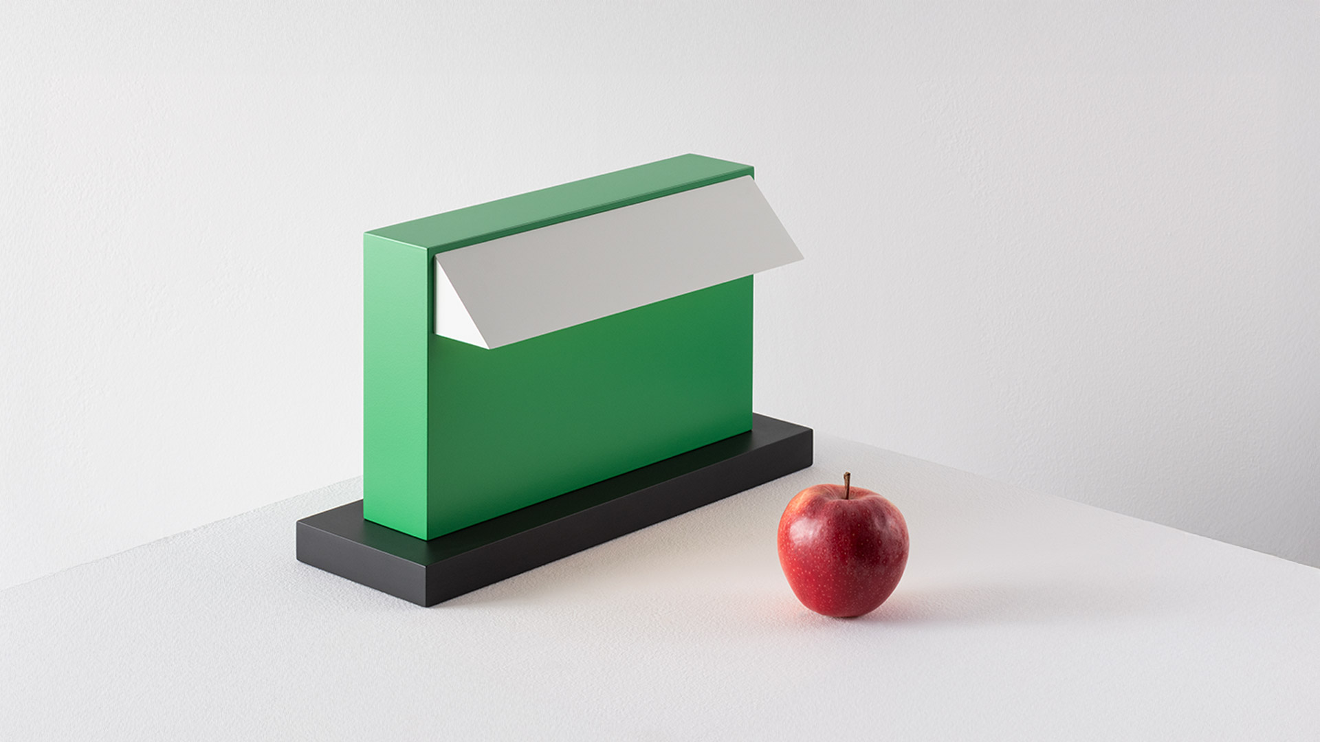 Artemide Hera table lamp in vibrant green with white diffuser on black base, illuminating a desk with notepad and pen