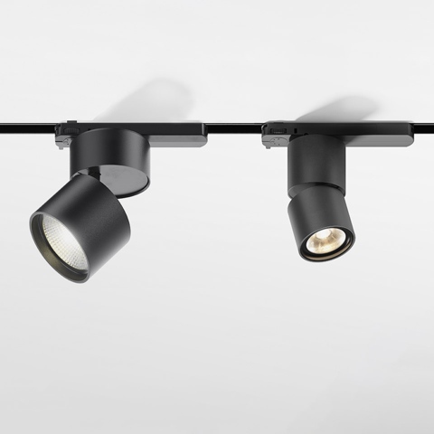 Two Artemide Hoy Spot black track lights mounted on a 3-phase rail, one tilted left illuminated, one facing forward lit