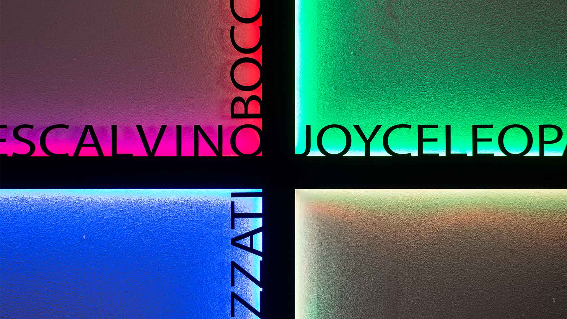 Four illuminated wall panels with colorful LED lighting in pink, green, blue, and white, displaying literary authors' names including Joyce, Calvino, and others.