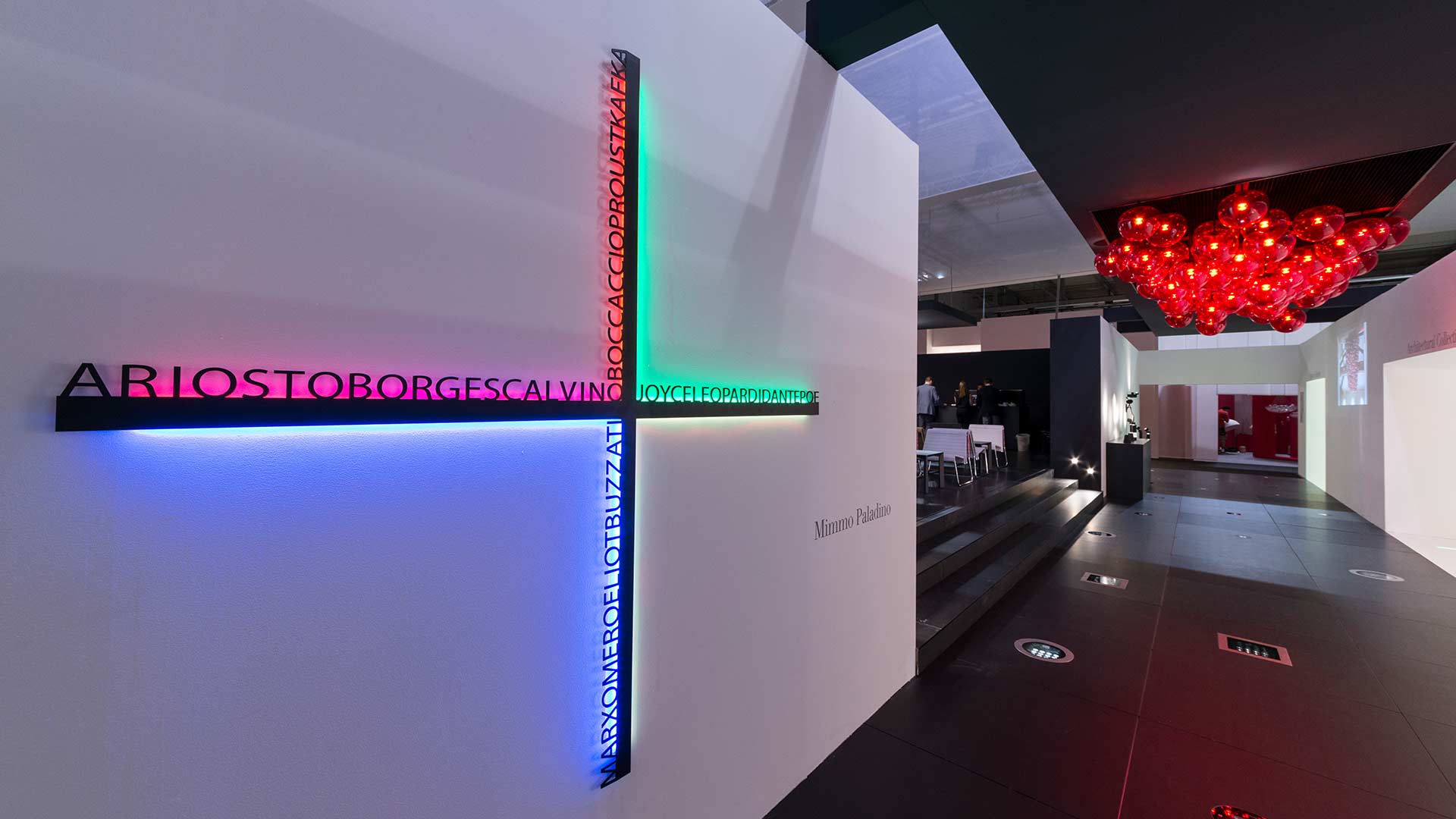 Artemide Hsiang installation: multicolored LED light bars forming a cross on a white wall, displaying text in vivid blue, green, and red hues