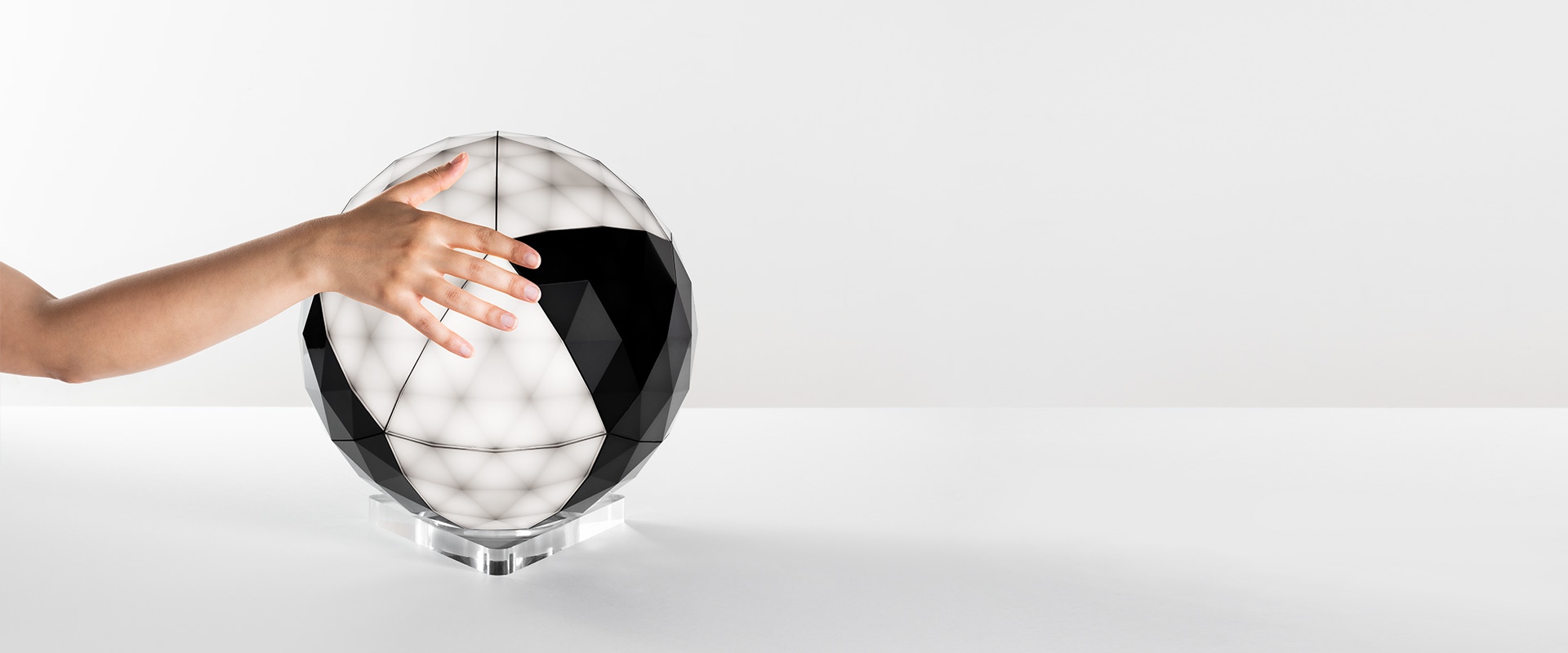 Artemide Huara table lamp: illuminated geometric sphere with triangular panels, USB charging port connected to a smartphone