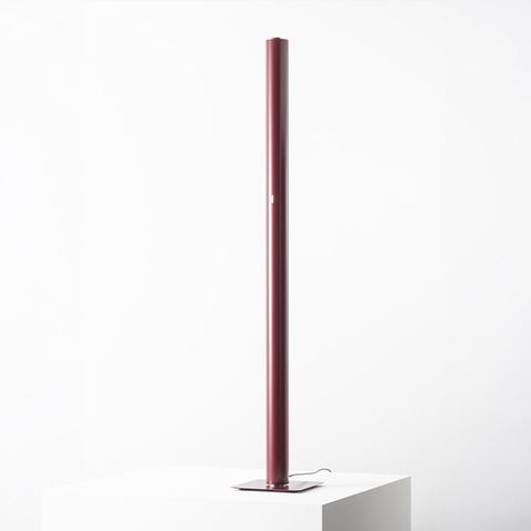 Artemide Ilio floor lamp: slim burgundy cylindrical LED column on a square flat base, emitting indirect ambient light