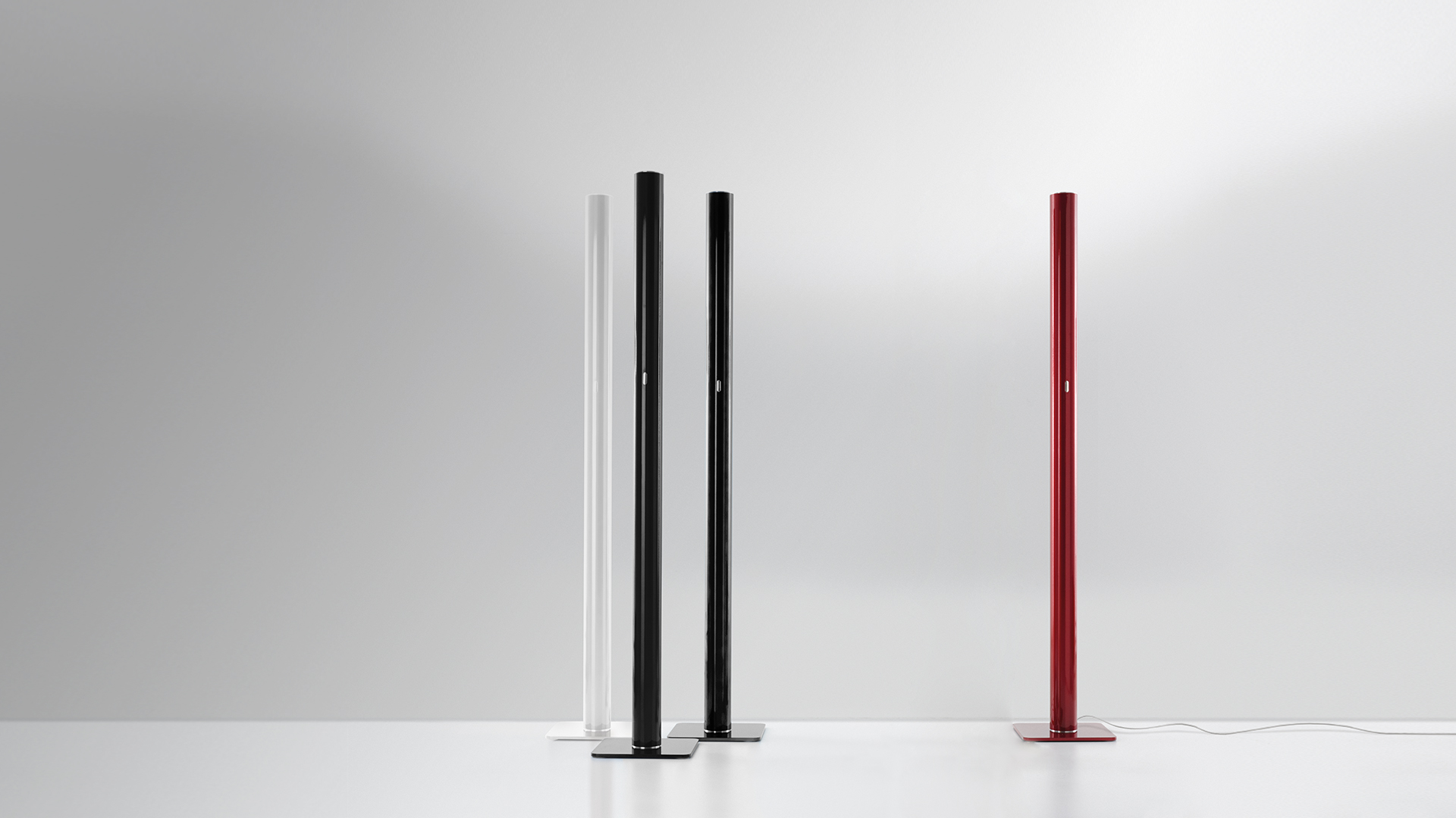 Artemide Ilio collection in burgundy: tall floor lamp, table lamps including Nessino, Tolomeo Micro, and decorative objects grouped on white pedestals