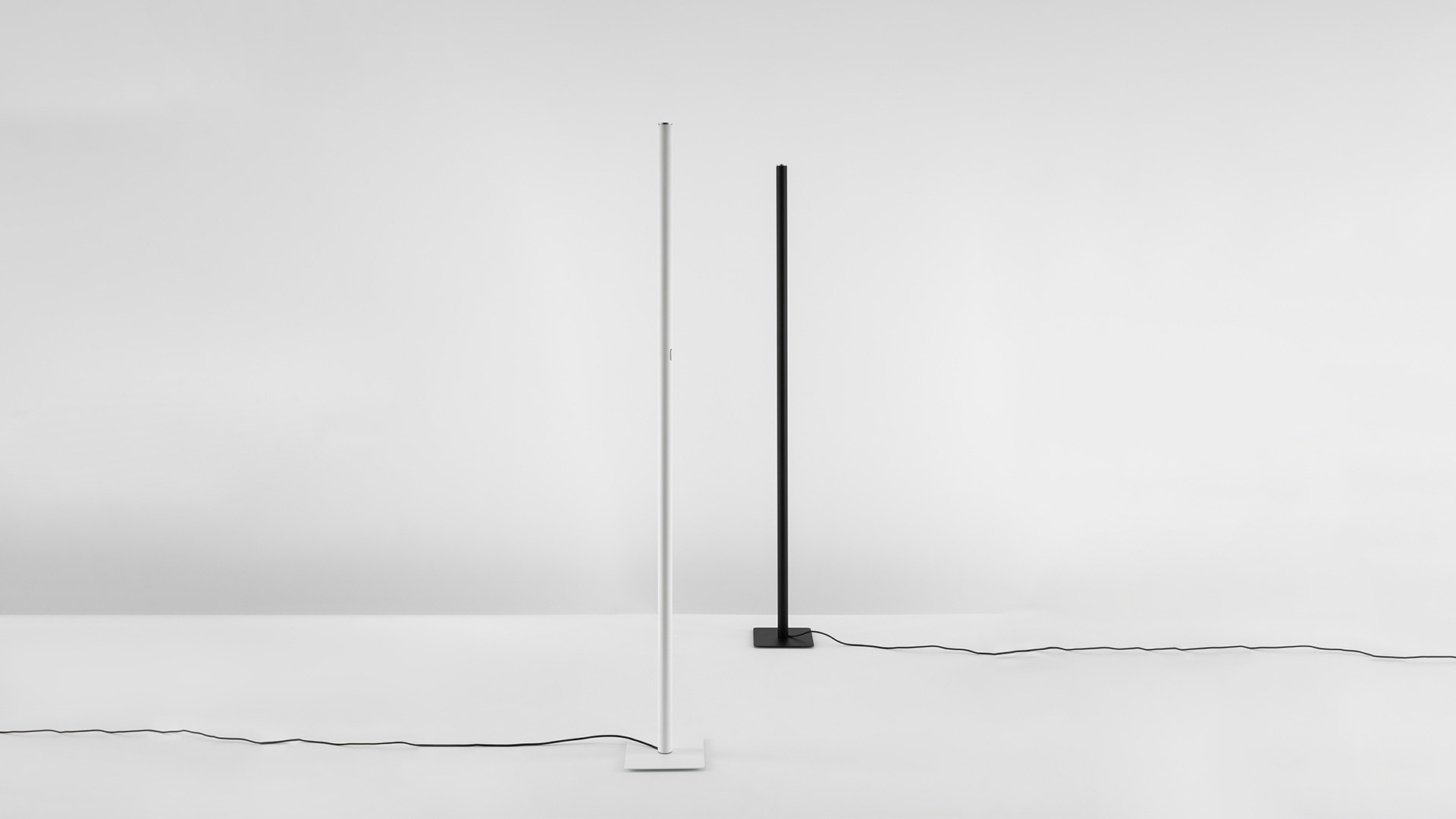 Artemide Ilio and Ilio Mini floor lamps: two cylindrical columns in black and white with recessed LED top emitter on red background