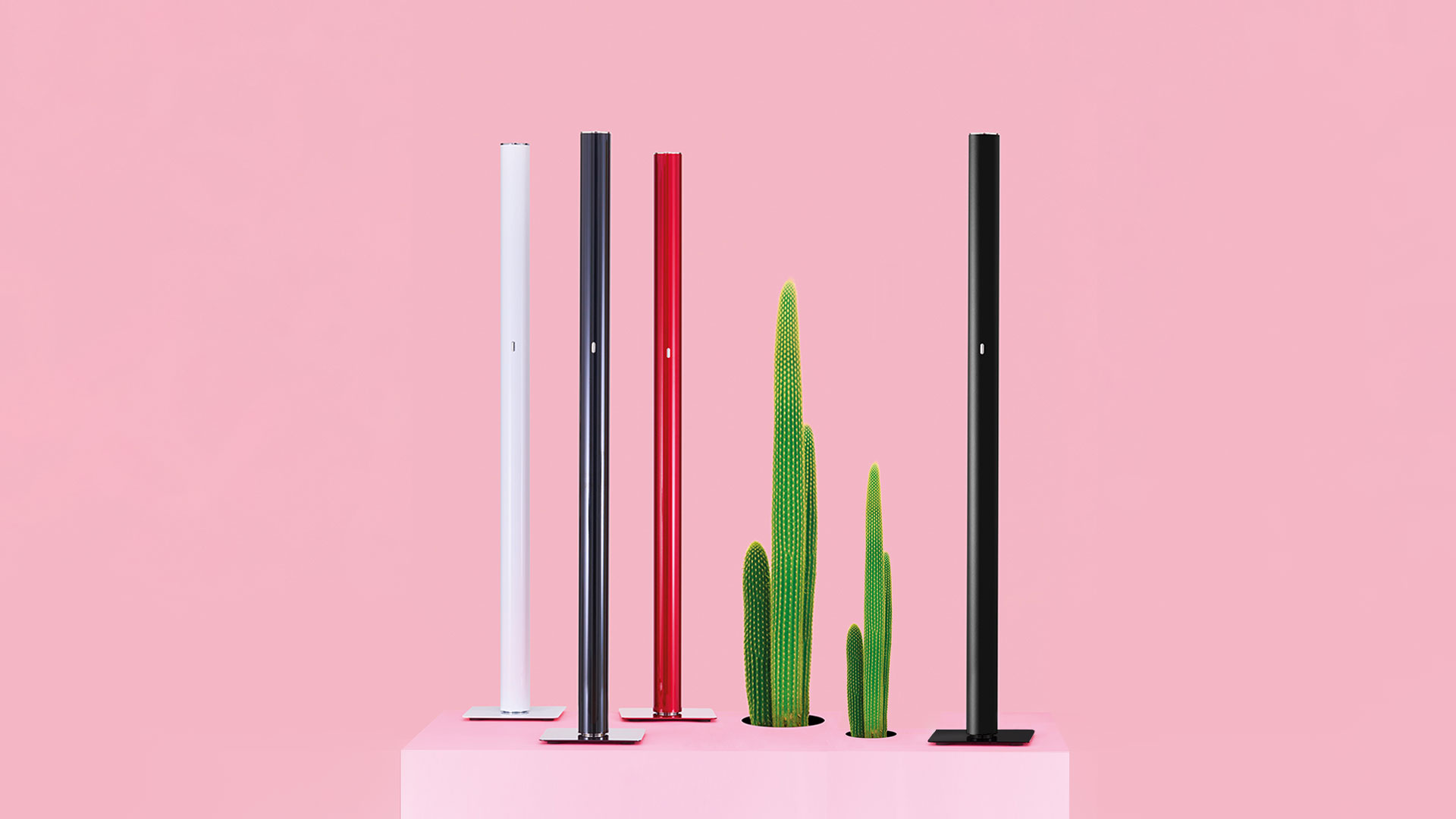 Three Artemide Ilio floor lamps in red, white, and black, featuring slim cylindrical columns on square bases in a minimalist white room