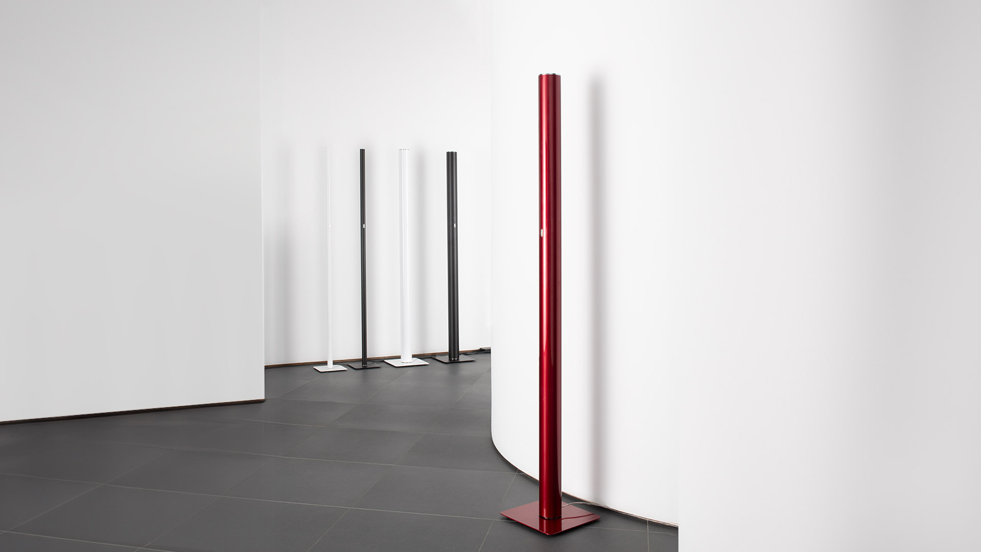 Four Artemide Ilio floor lamps in white, red, and black, displayed alongside green cacti on a pink background