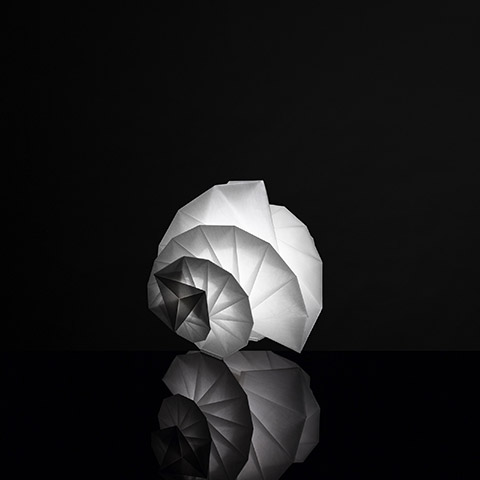 Artemide In-Ei Mendori by Issey Miyake: glowing origami-inspired spiral table lamp in white recycled material, reflected on dark surface