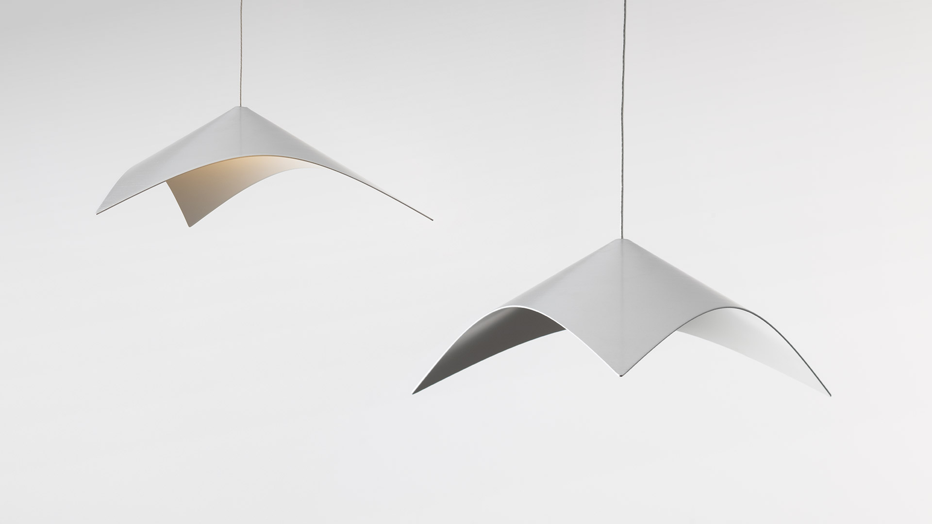 Two Artemide Iperbole pendant lamps with white sculptural curved shades suspended from thin cables against a white background