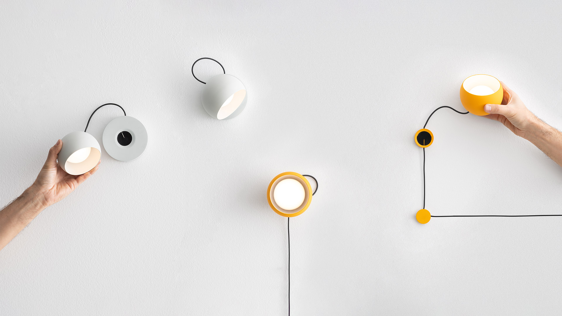 Two Artemide Ixa wall lamps: left white dome shade with black hook, right yellow ring shade with black cord and yellow dimmer ball