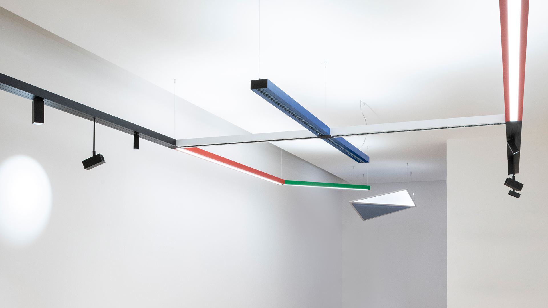 Artemide Katà Métron modular ceiling lighting system with colored linear profiles in blue, green, red, and black with adjustable spotlights.