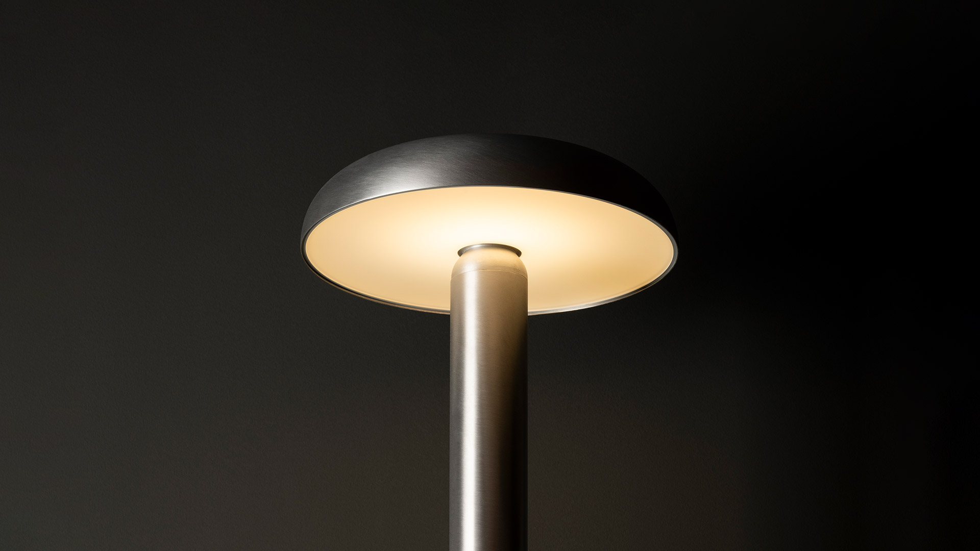 Artemide Knop table lamp: slim gold stem topped by a wide flat disc shade in dark metal emitting warm diffused light