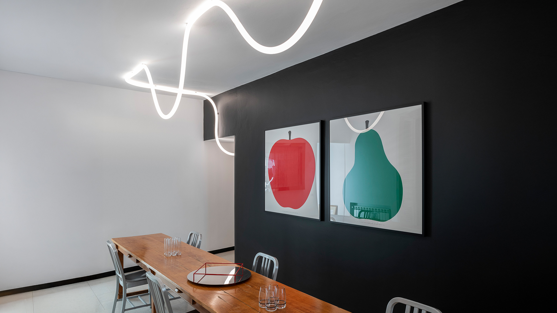 Modern office lounge with Artemide La Linea circular pendant light illuminating a seating area with blue chairs and lush greenery