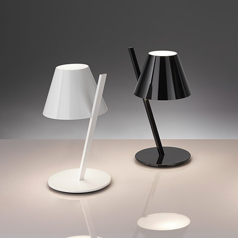 Artemide La Petite Table lamps in white and black, featuring angled stems, conical shades, and circular bases on a reflective surface