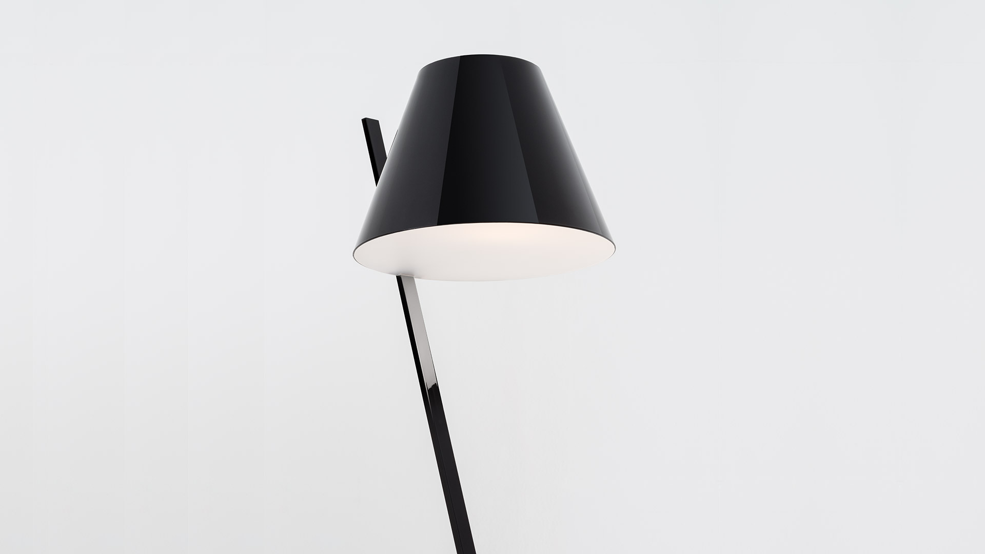 Artemide La Petite Floor lamp: sleek black conical shade on angled black stem, emitting warm diffused light from base