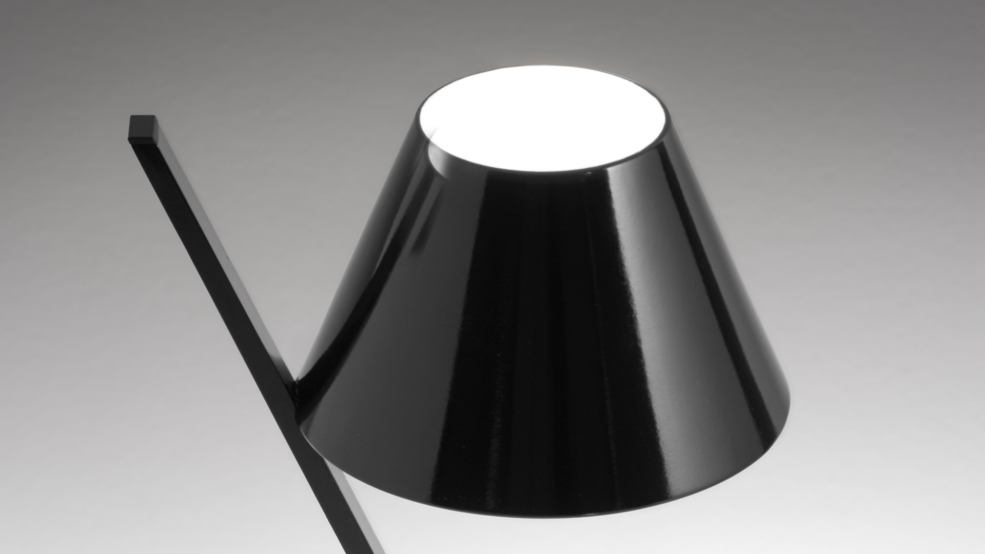 Modern bedroom with blue-grey wall, light wood bed frame, white bedding, and a small Artemide La Petite Table lamp on the nightstand