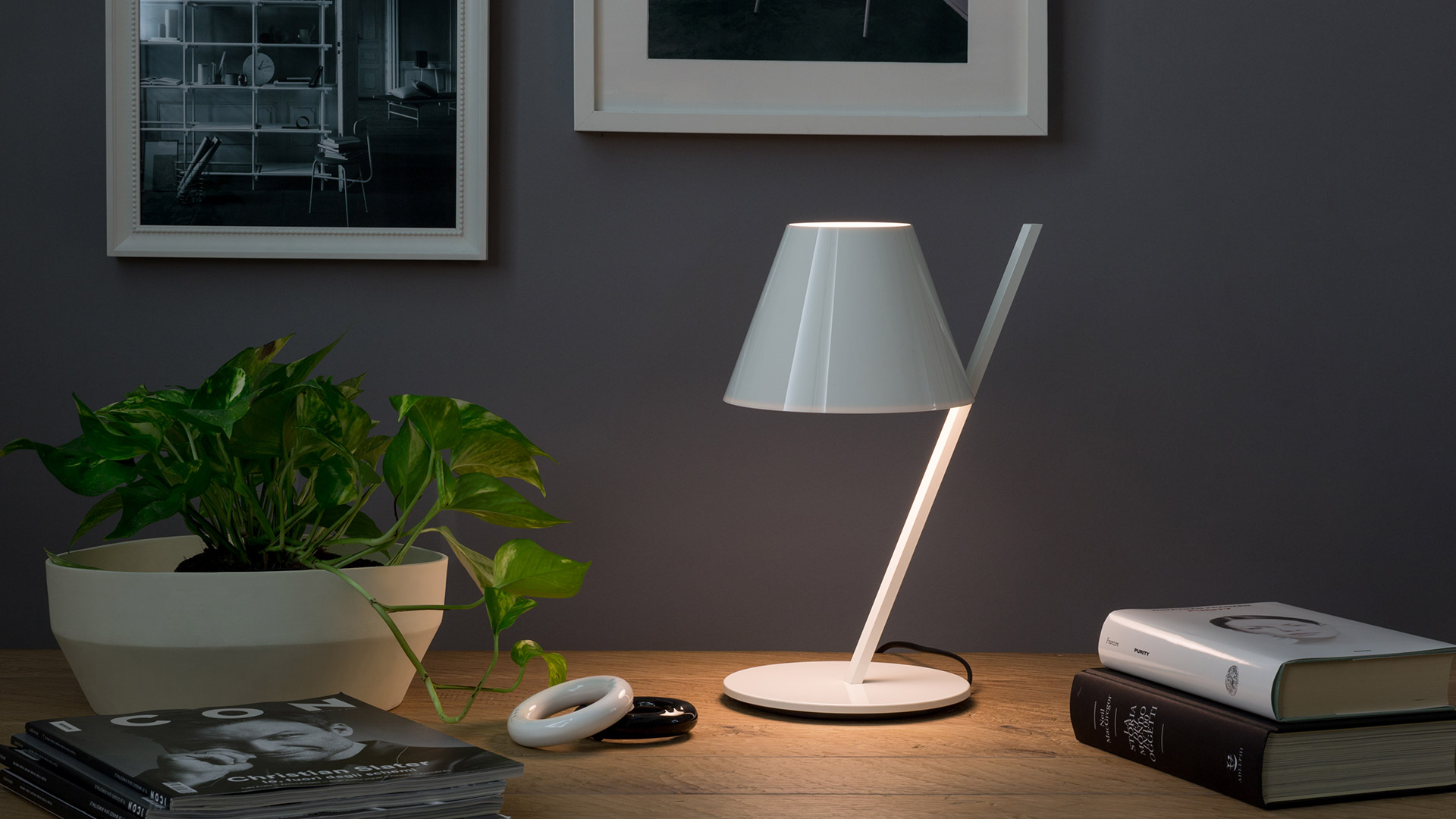 Artemide La Petite Table lamp: glossy black conical shade on a diagonal black stem, with white interior diffuser.