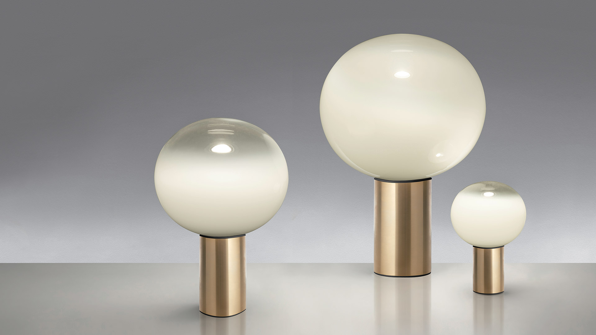 Artemide Laguna Tavolo table lamp with frosted spherical glass diffuser on a brass and black metal base, emitting warm light