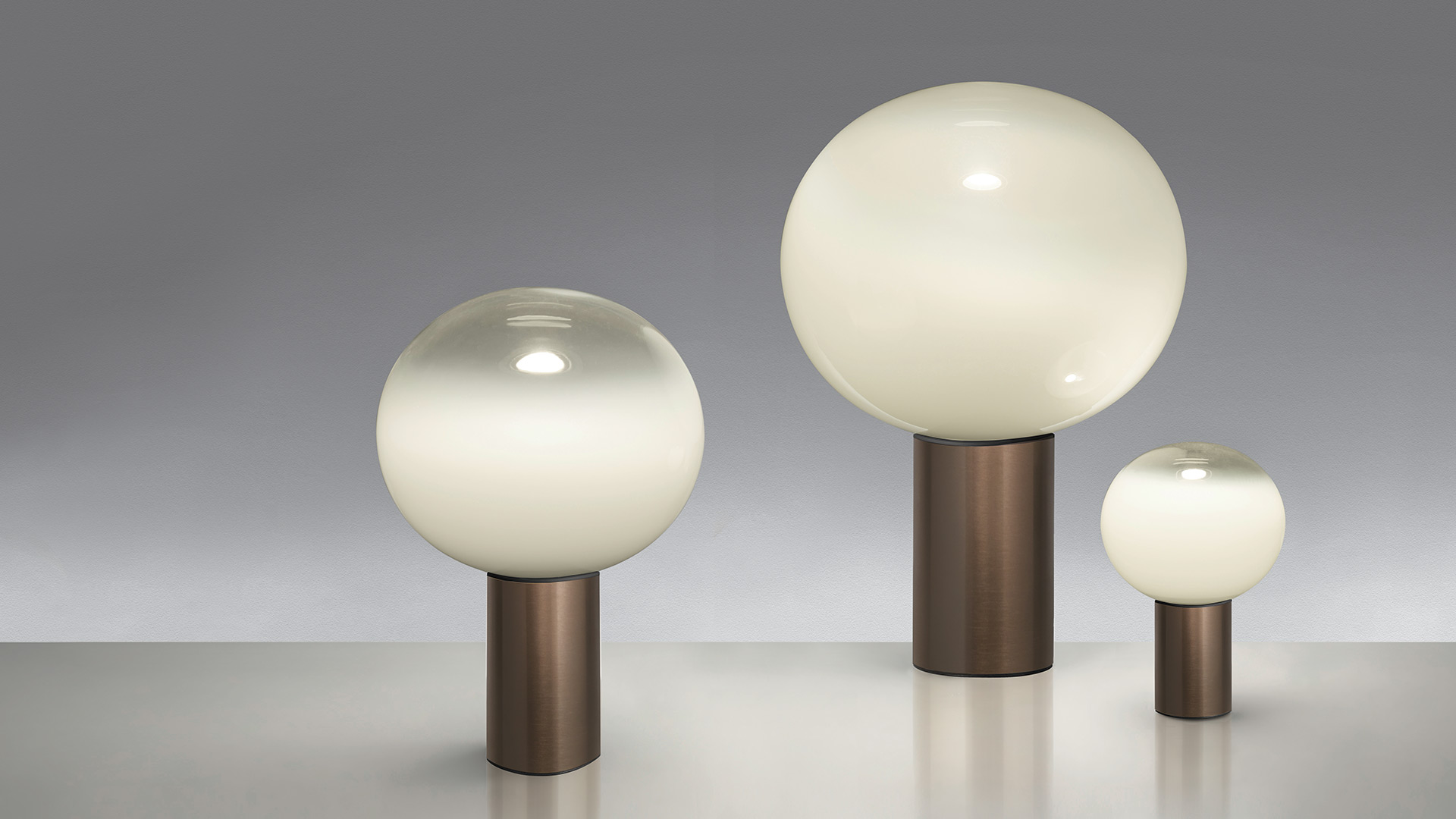 Two Artemide Laguna Tavolo table lamps with opal glass spheres on dark bases, placed on white side tables beside a pink armchair