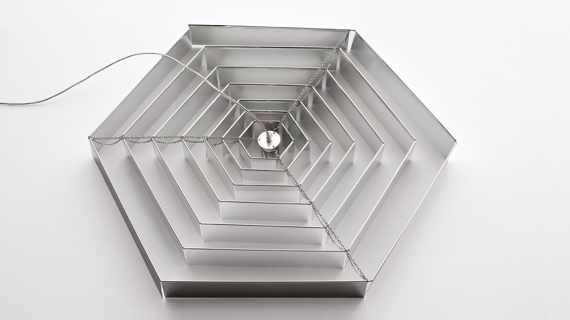 Two Artemide Lampada Esagonale pendant lights with layered hexagonal aluminum shades in white and chrome finish, suspended by steel cables.