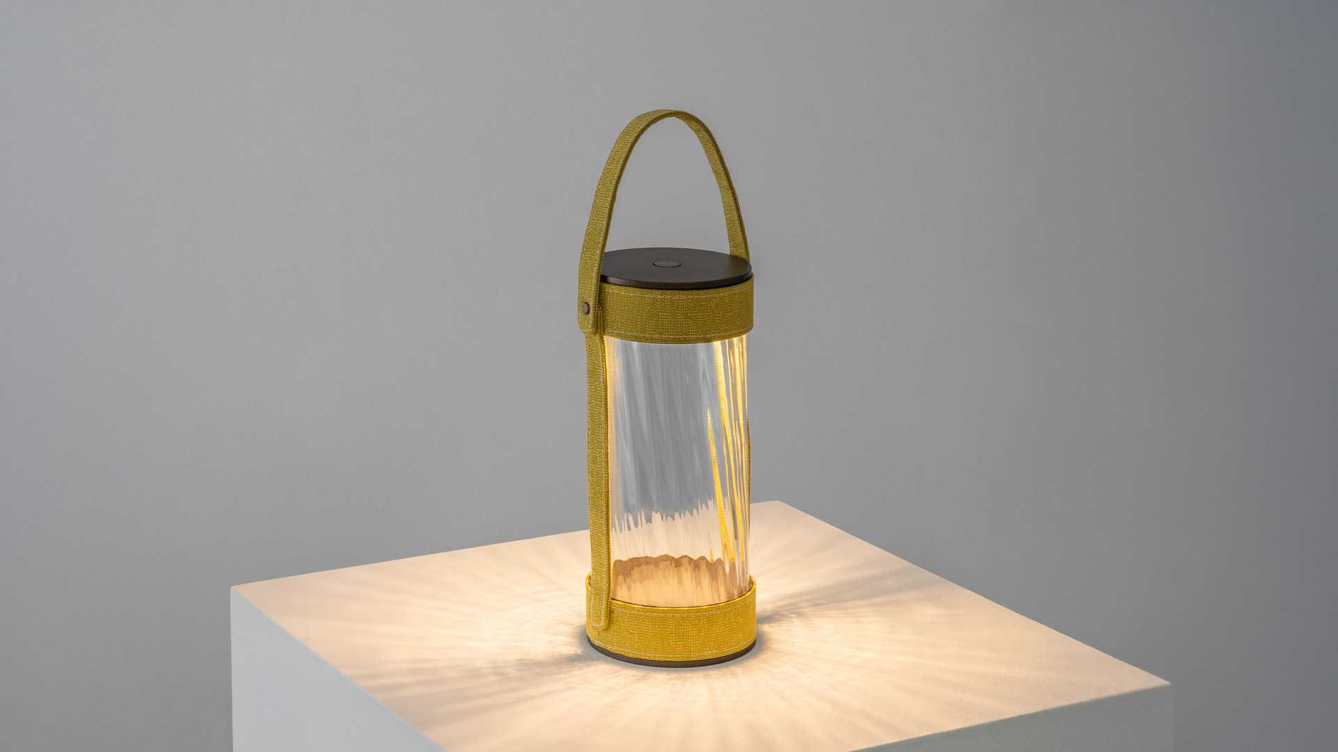 Close-up of Artemide Laya portable lamp: cylindrical dark body with terracotta woven textile strap and brass rivet detail