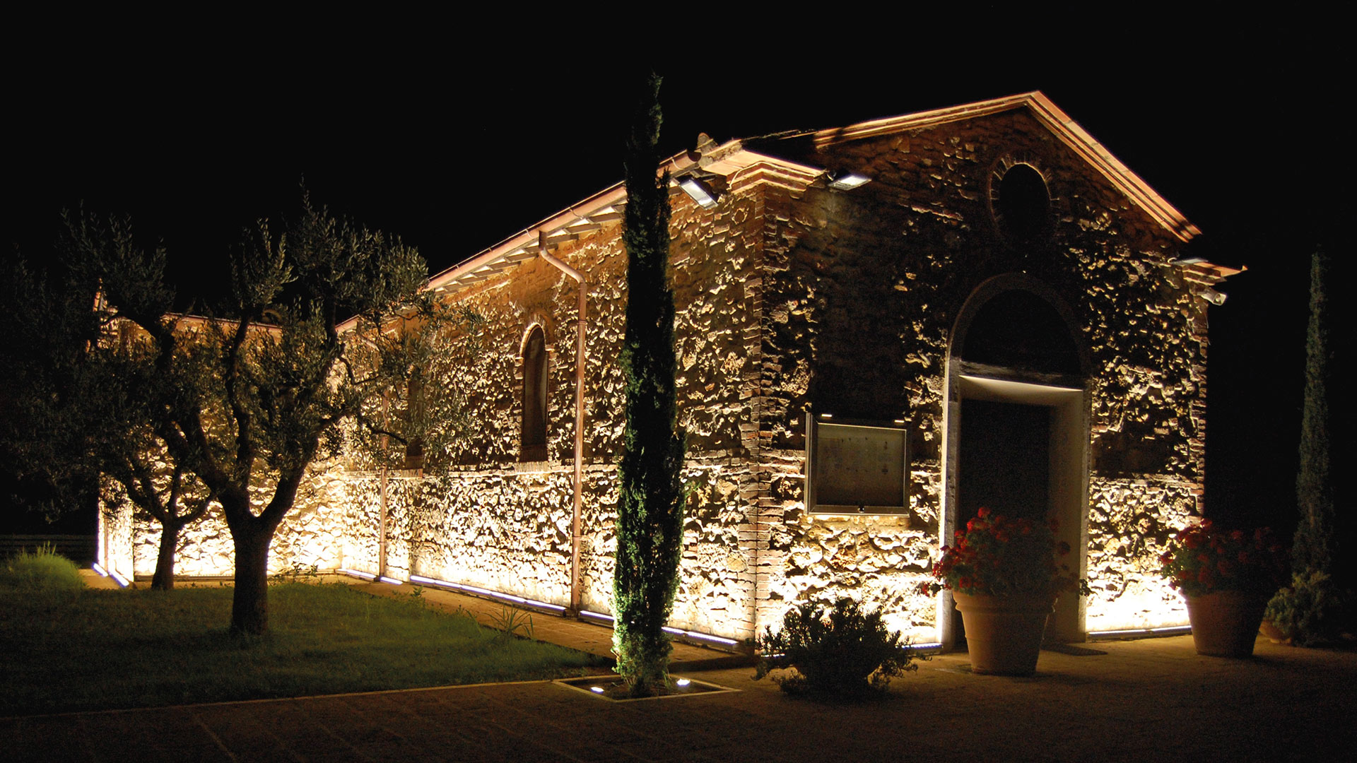 Historic stone chapel illuminated at night by Artemide LineaLed Wallwasher fixtures, casting warm golden light across textured walls and garden