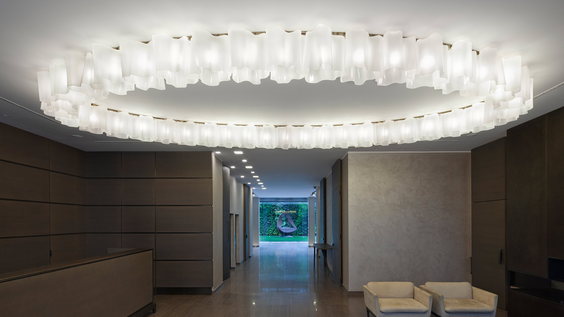 Logico Soffitto by Artemide: two large oval ceiling fixtures with frosted glass diffusers illuminate an elegant lobby corridor