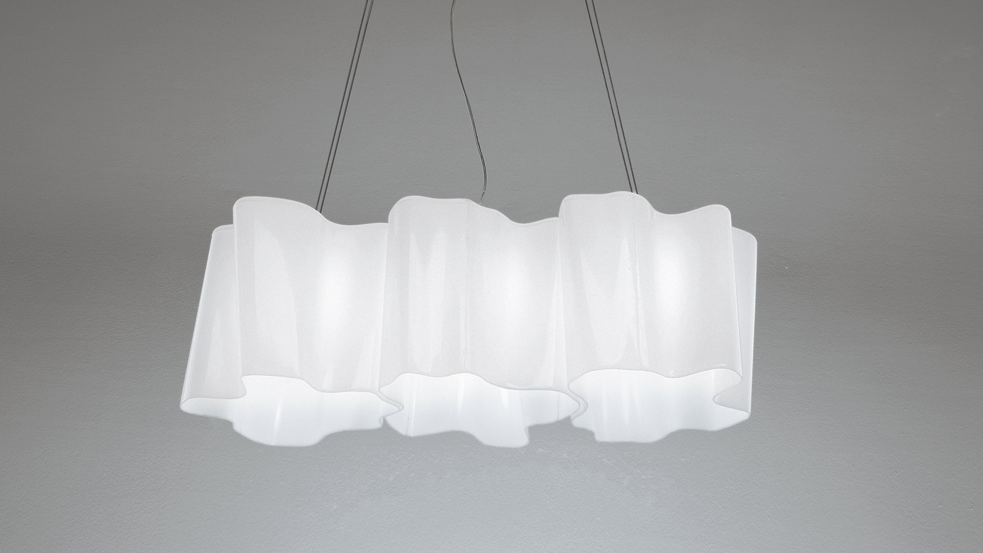 Artemide Logico suspension 3 in linea: three connected white diffusers with soft wavy edges, hanging from thin cables