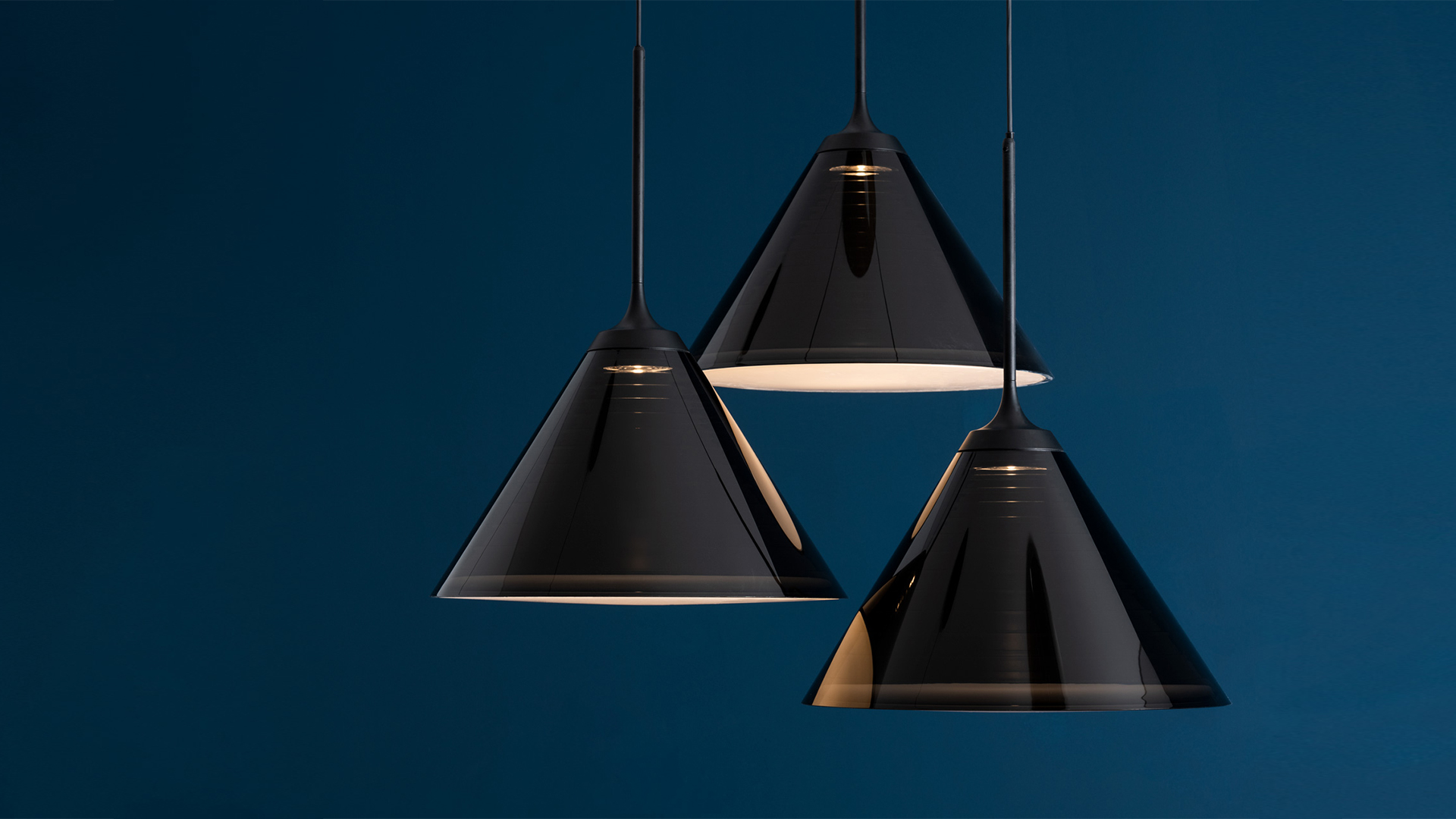 Three Artemide Look at Me pendant lamps with glossy black conical shades hanging on black cords against a dark blue background
