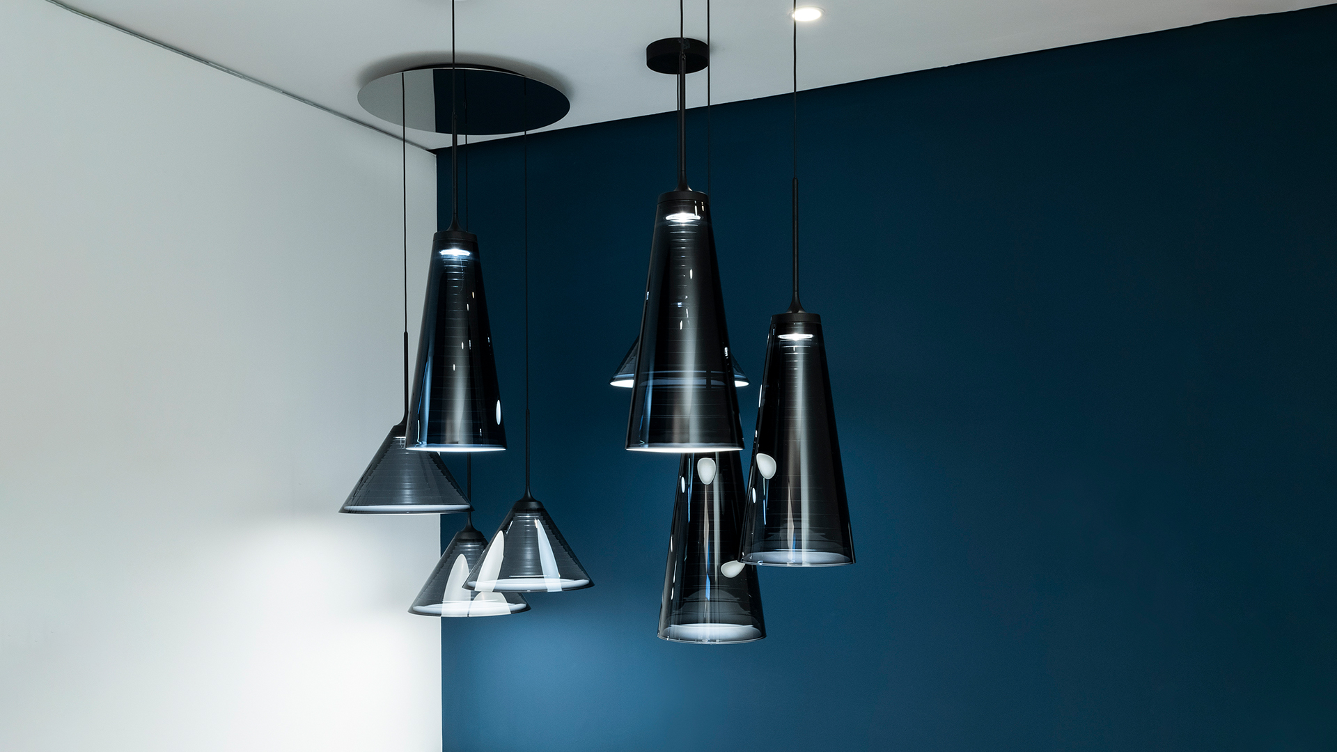 Three Artemide 'Look at Me' black conical pendant lamps hanging at different heights against a deep blue background