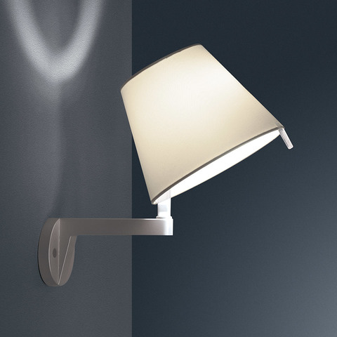 Artemide Melampo Parete wall lamp with cream fabric shade on brushed aluminum bracket, casting decorative light pattern on wall