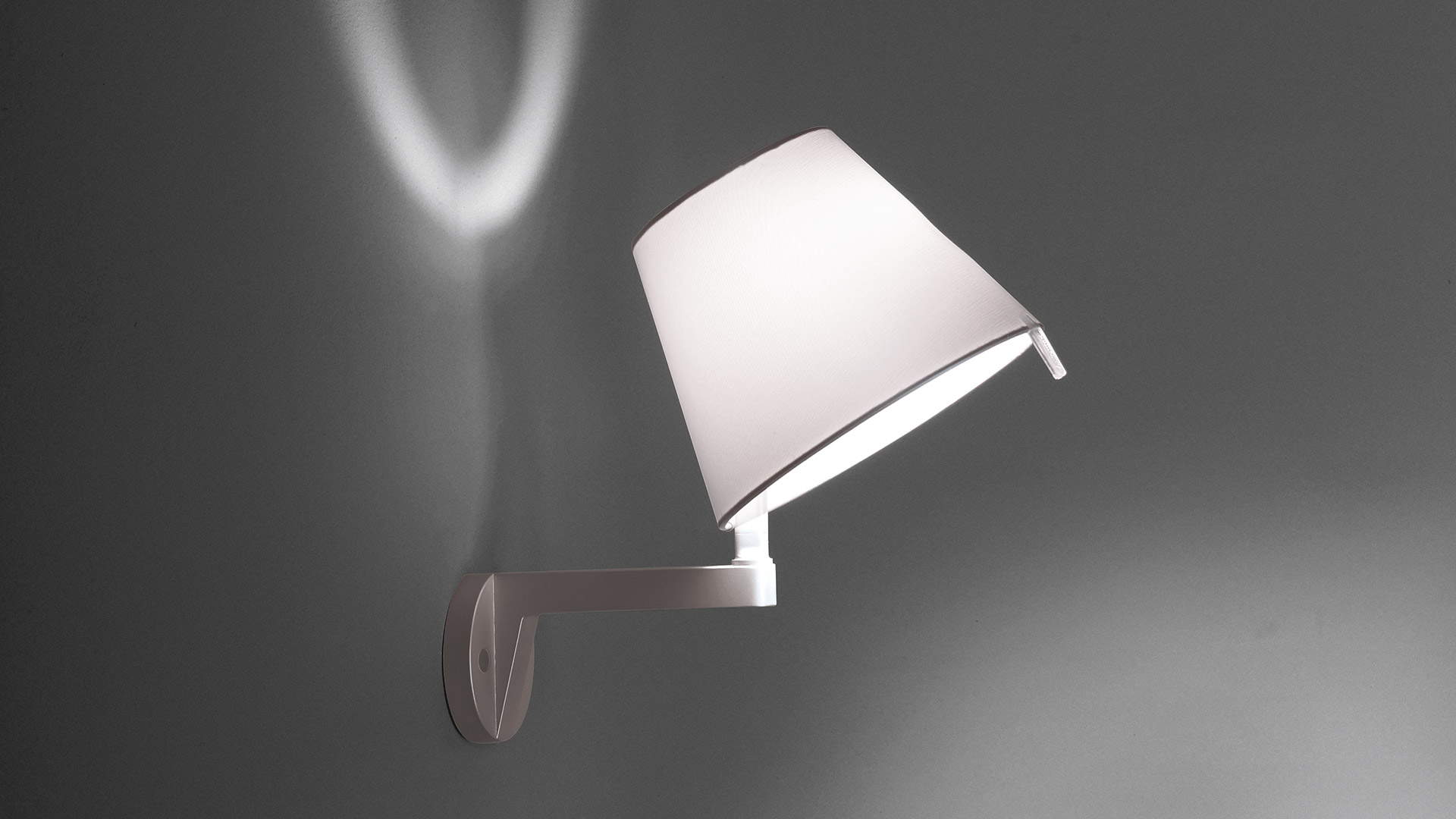 Melampo Parete wall lamp by Artemide, white conical shade on dark headboard, casting warm decorative light in a bedroom