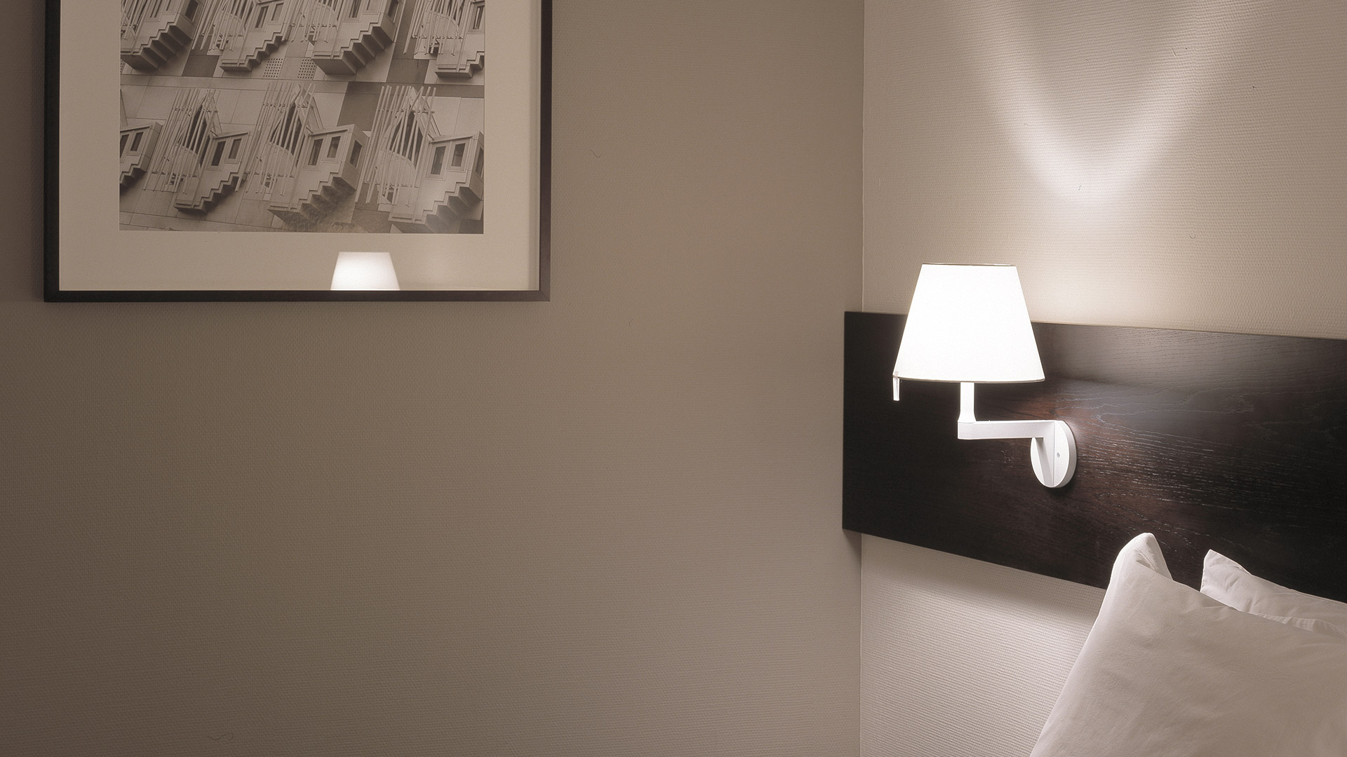 Artemide Melampo Parete wall lamp in white, featuring a conical fabric shade on an angular arm, casting warm light on the wall.